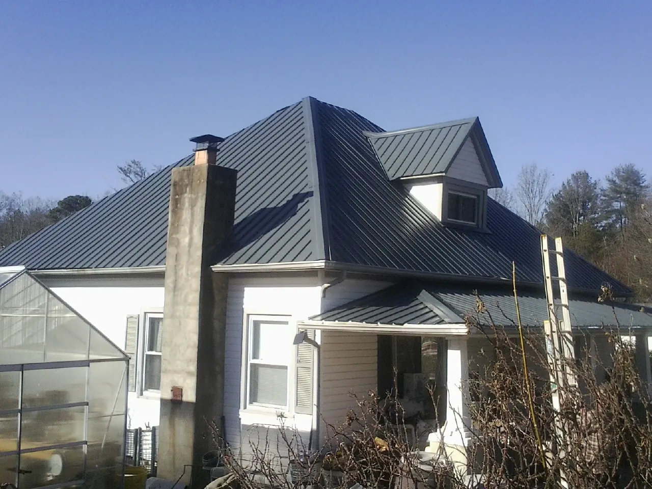 Dark blue standing seam metal roof on a white farmhouse with dormer — Slate & Tile Roof Repair by Roofing Brothers in Holmesville