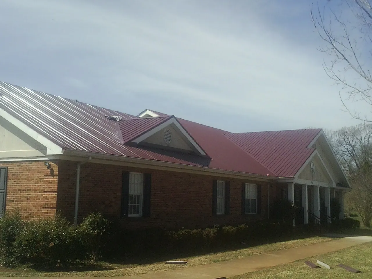 Red metal roof with gabled entries on a long brick building, from a Hail Damage Roof Repair job in Holmesville