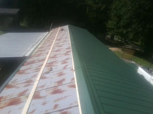 Old rusted panels beside newly installed green metal roofing — Wind Damage Roof Repair by Roofing Brothers in Holmesville