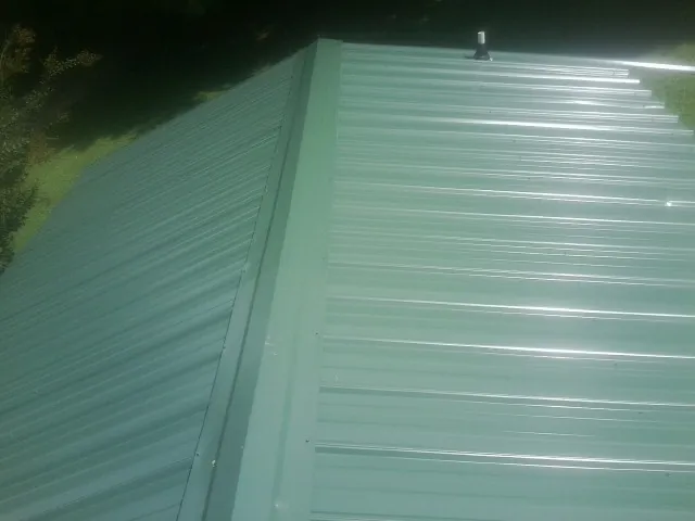 New green metal panels meeting at the ridge of a roof — Flat Roof Repair work by our crew in Holmesville