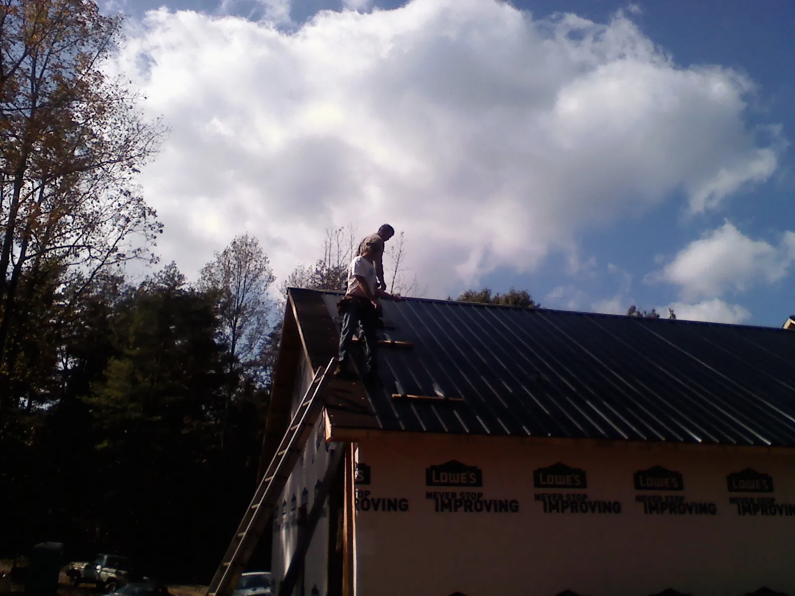 Roofer fastening dark metal panels high against a cloudy sky, from a Roof Inspection job in Holmesville