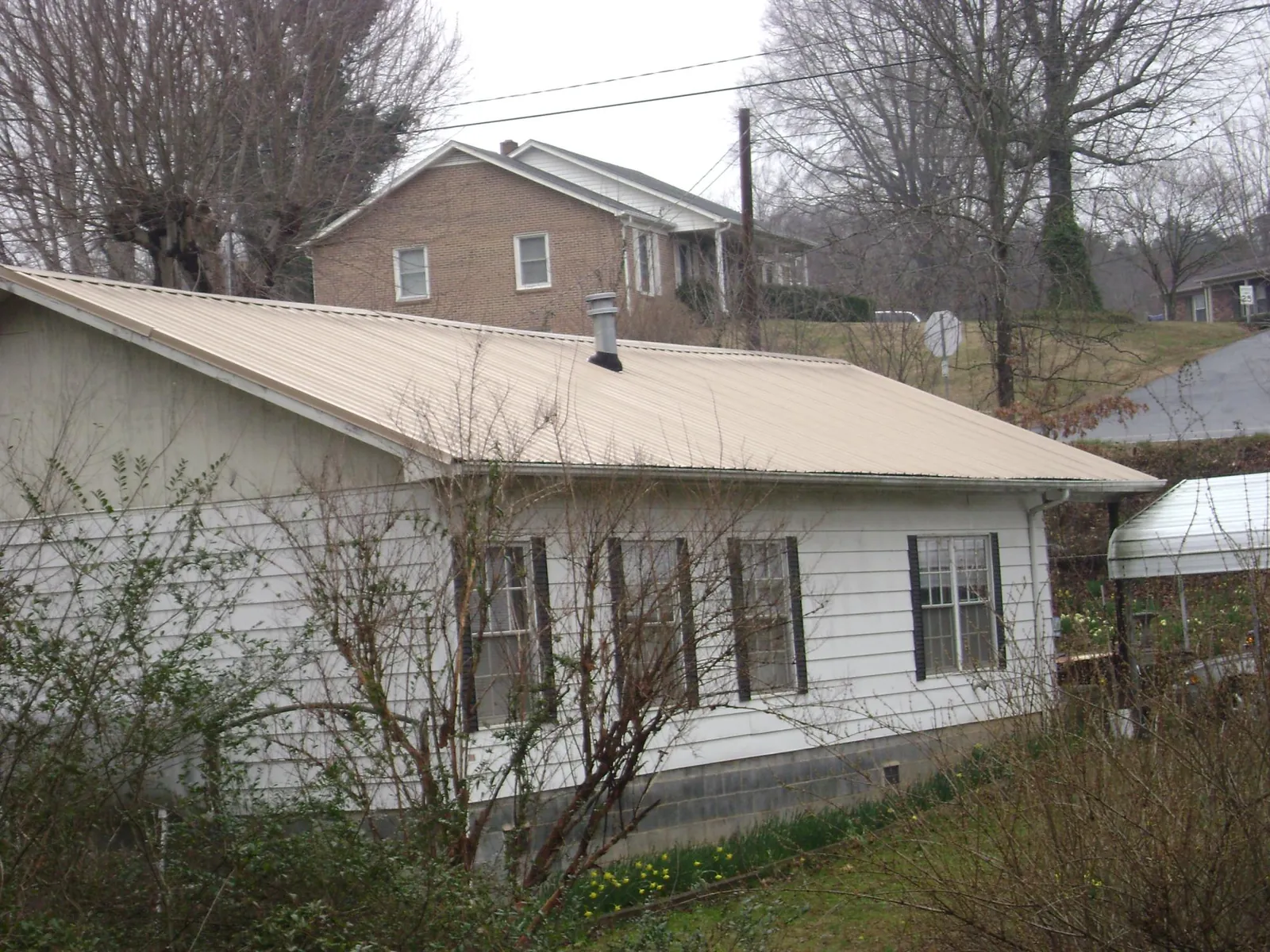 Tan metal roof on a white sided house set into a hillside — Commercial Roofing by Roofing Brothers in Holmesville