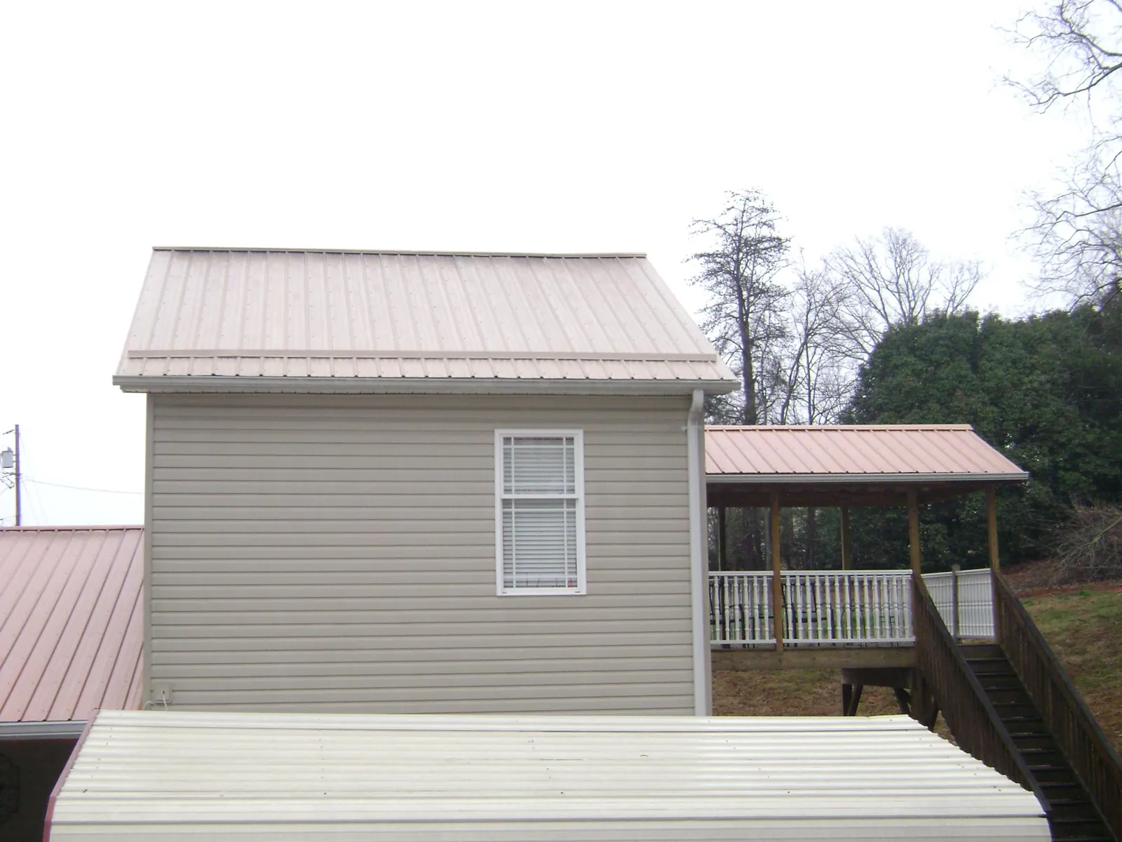 Tan metal roofs on a two story addition and attached porch, from a Roof Replacement job in Holmesville
